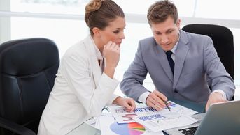 Two professionals analyzing charts and data at a glass table.