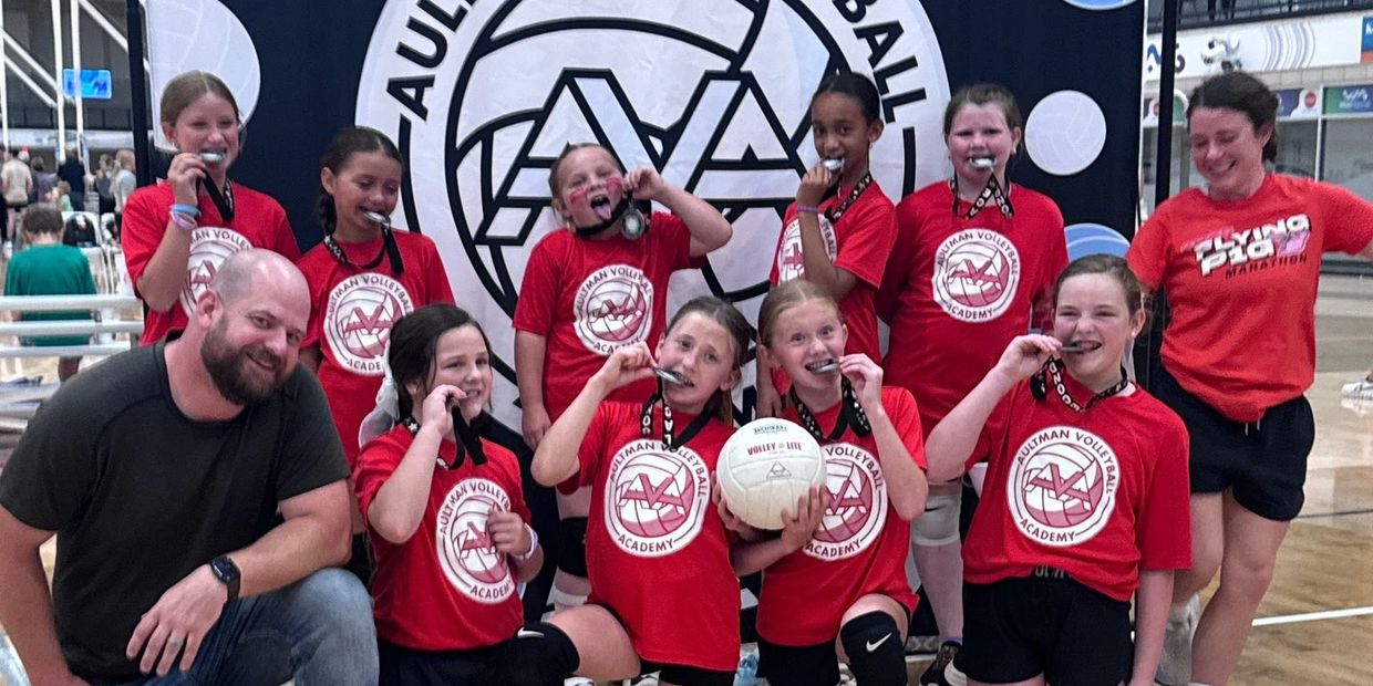Youth volleyball team celebrating with medals and volleyball.