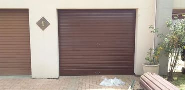 Closed brown garage doors with a number 1 plaque and plants nearby.