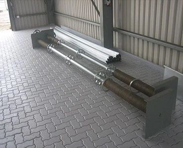 Two large industrial metal bolts with nuts and plates on a tiled floor.