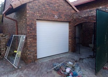 Newly installed white garage door on a brick house with construction debris nearby.