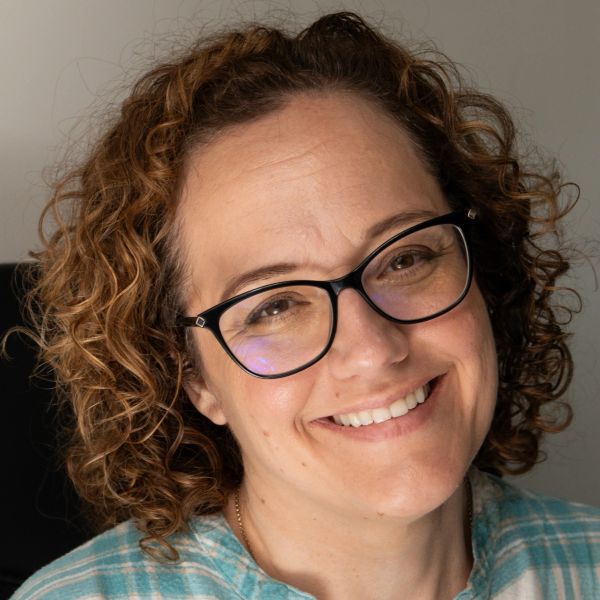 Smiling woman with curly hair and glasses.