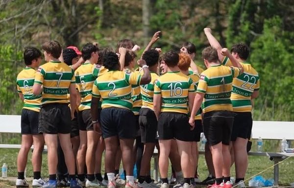 Youth rugby team in green and yellow striped jerseys huddling outdoors.