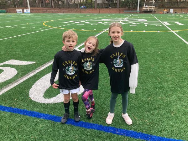 Three kids in matching Exiles Rugby shirts stand on a sports field.