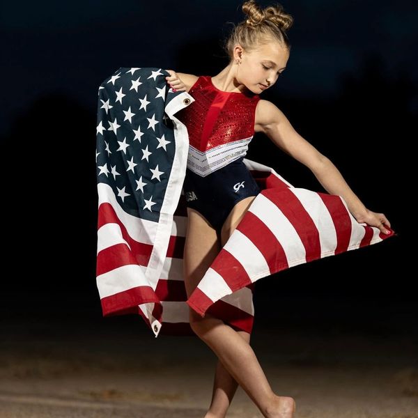 Preteen gymnast poses in red white blue leotard with American flag.
