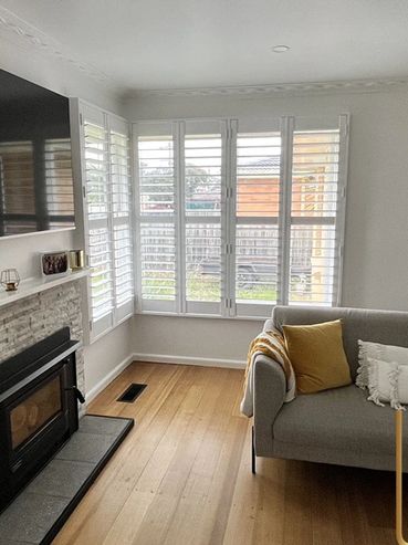 We installed these sleek white plantation shutters in a corner living room featuring a fireplace and