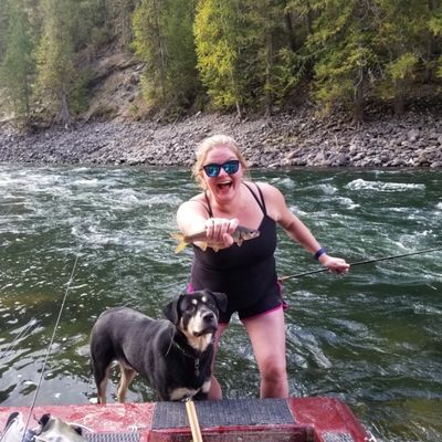Woman holding a fish by a river with her dog.