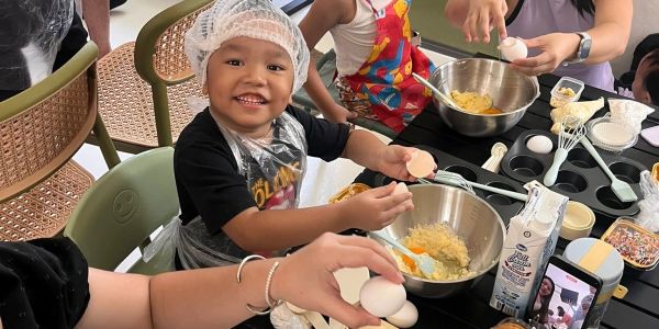 A child joyfully cracks an egg while baking with family.