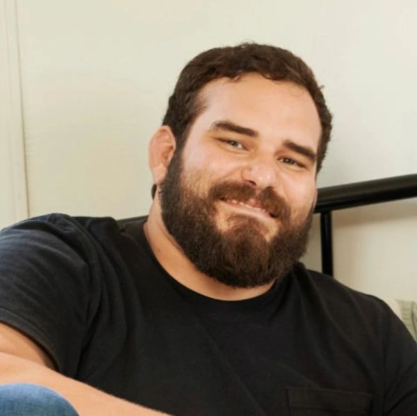 Bearded man smiling warmly while seated indoors.