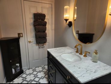 Elegant bathroom with marble countertop, gold fixtures, and dark cabinetry.