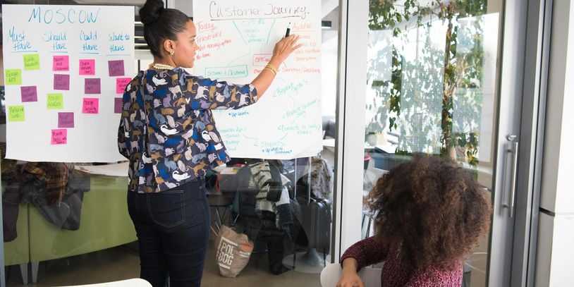 Two women discussing business strategies and writing onto paper on a wall