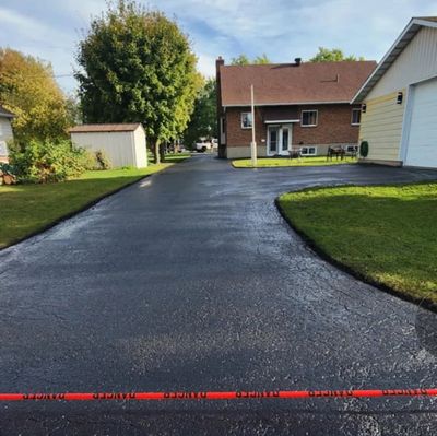 Freshly paved driveway in a suburban neighborhood with houses and greenery.
