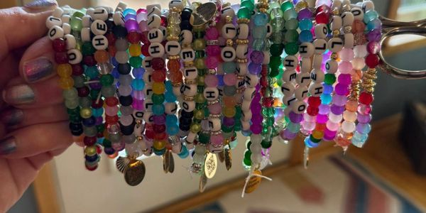 Hand holding colorful beaded bracelets with letter beads and charms.