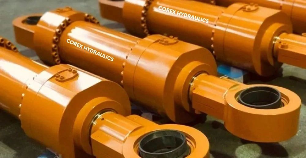 Orange hydraulic cylinders labeled COREX HYDRAULICS placed on the floor.