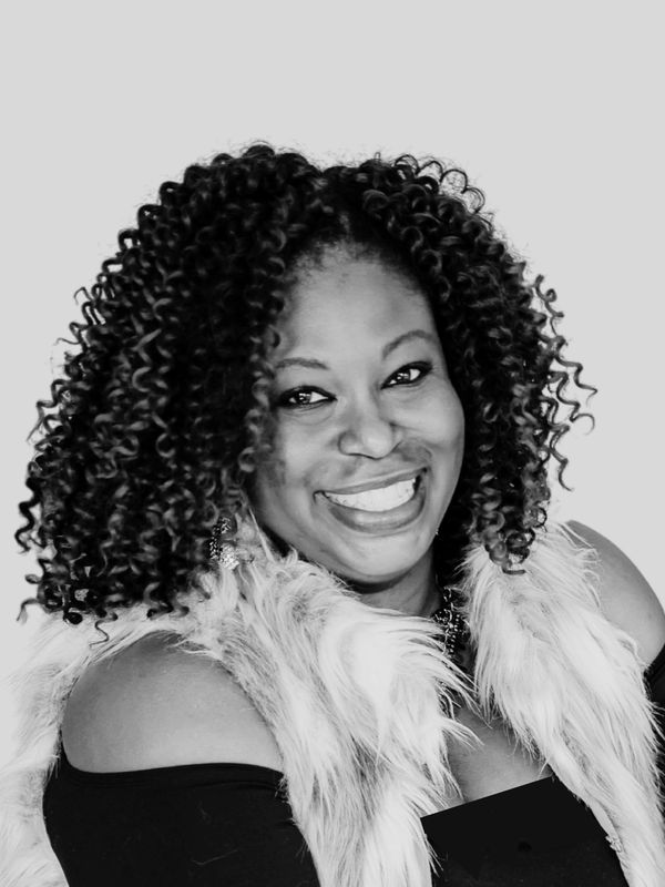 Smiling woman with curly hair and fur vest.