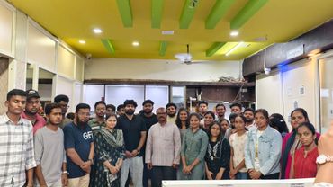 A diverse group of young adults and a few older individuals posing indoors under a yellow ceiling.