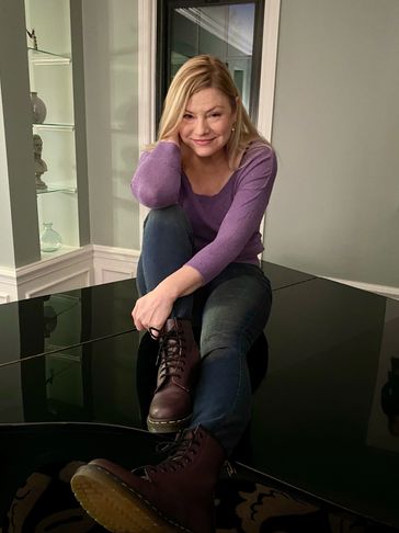 A woman in a purple sweater sitting on a black surface, smiling.