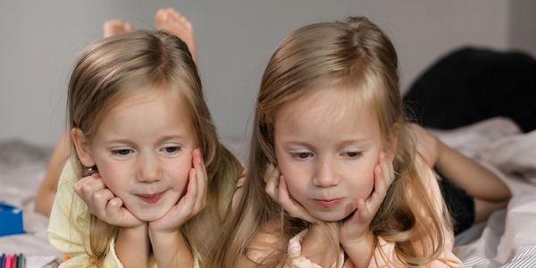 Two young girls lying on beds, resting their chins on their hands.