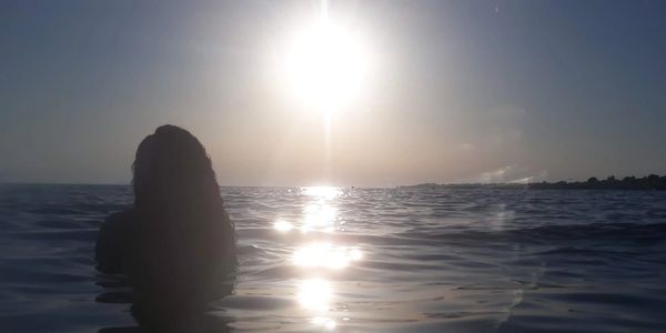 Silhouette of a person in the ocean during sunset with sun reflections on water.