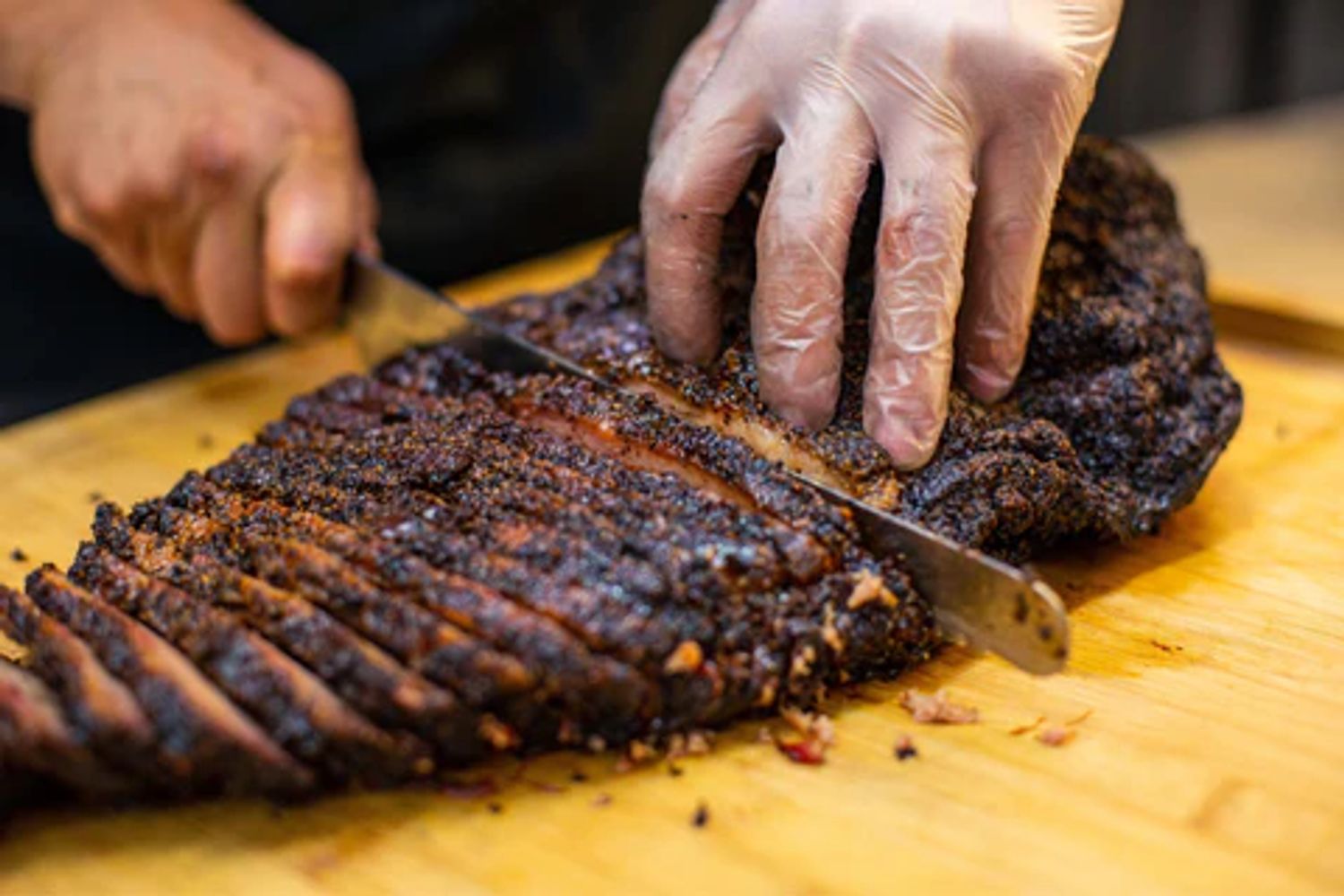 Person slicing a large, seasoned smoked brisket on a wooden board.