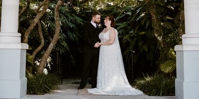Bride and groom holding hands under a leafy archway.