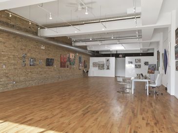 Spacious art gallery with diverse paintings on brick and white walls.