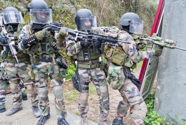 Soldiers in camouflage gear aiming rifles during a tactical exercise.