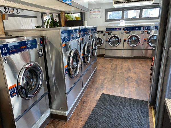 Interior of a clean laundromat with stainless steel washing machines and wood flooring.