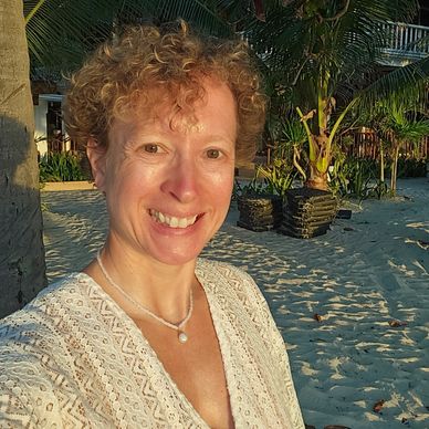 Frau mit lockigem Haar lächelt im Sonnenlicht am Strand.