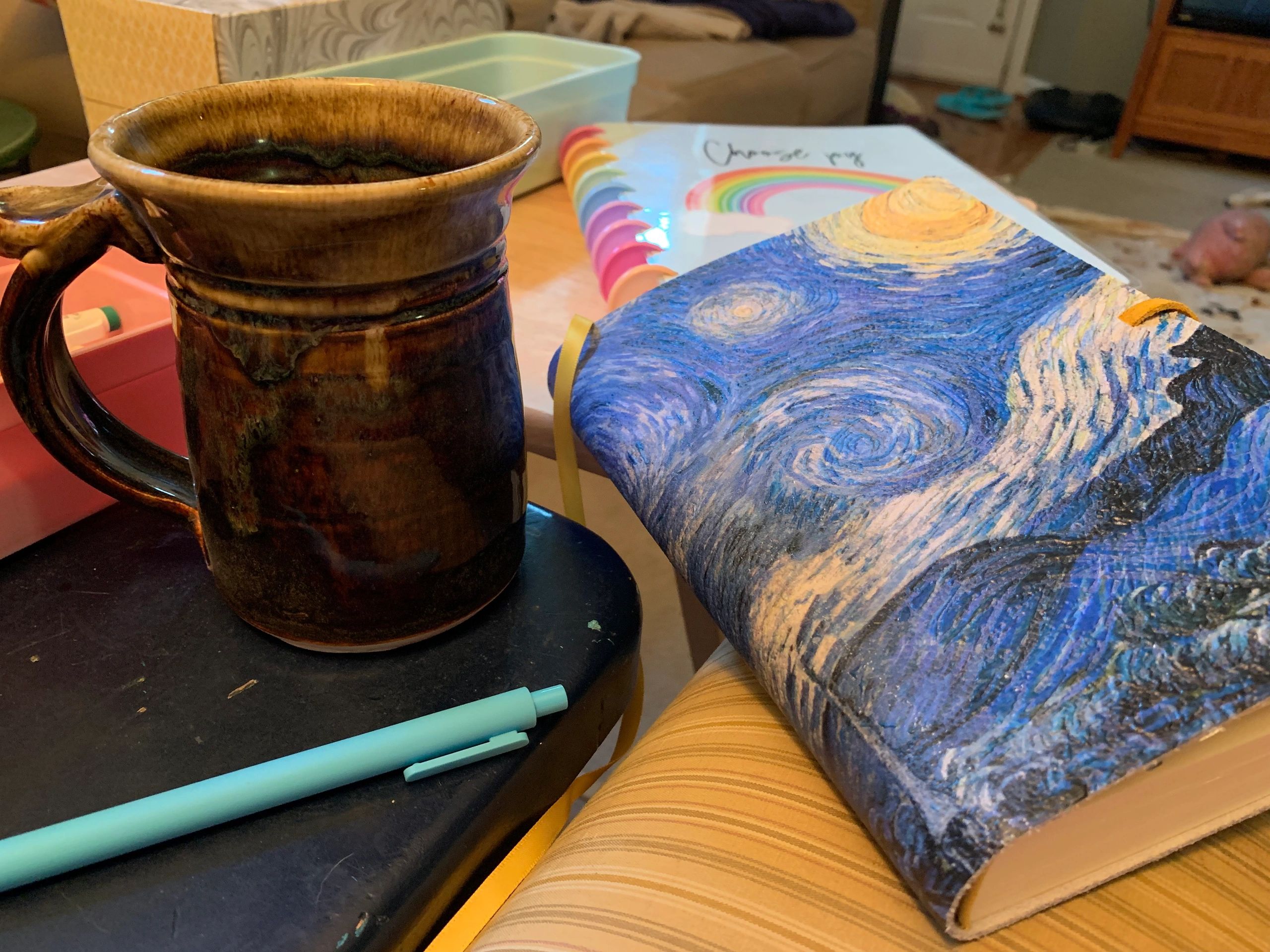 A brown ceramic mug, colorful notebooks, and a blue pen on a cozy table setup.
