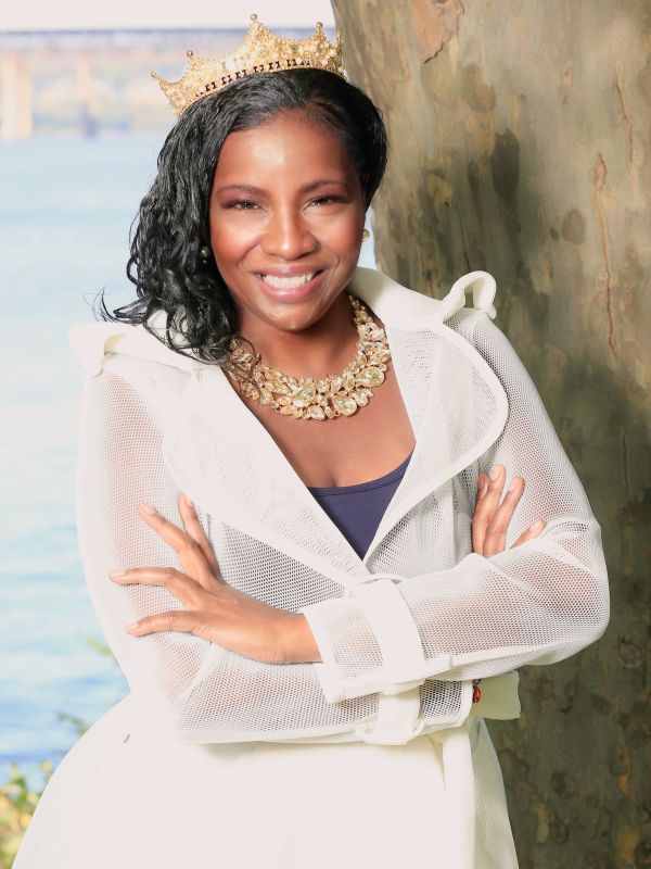 Woman smiling with a crown and necklace outdoors.