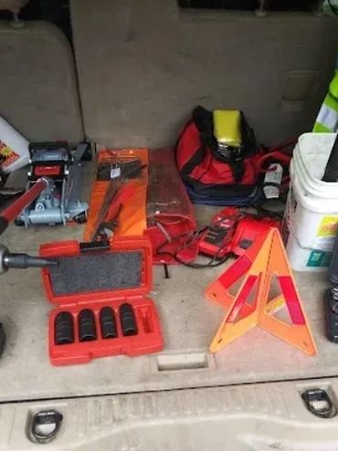 A collection of automotive tools and safety equipment in a vehicle trunk.