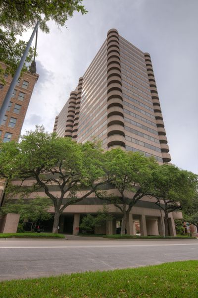Tall office building with rounded balconies and green trees in front.