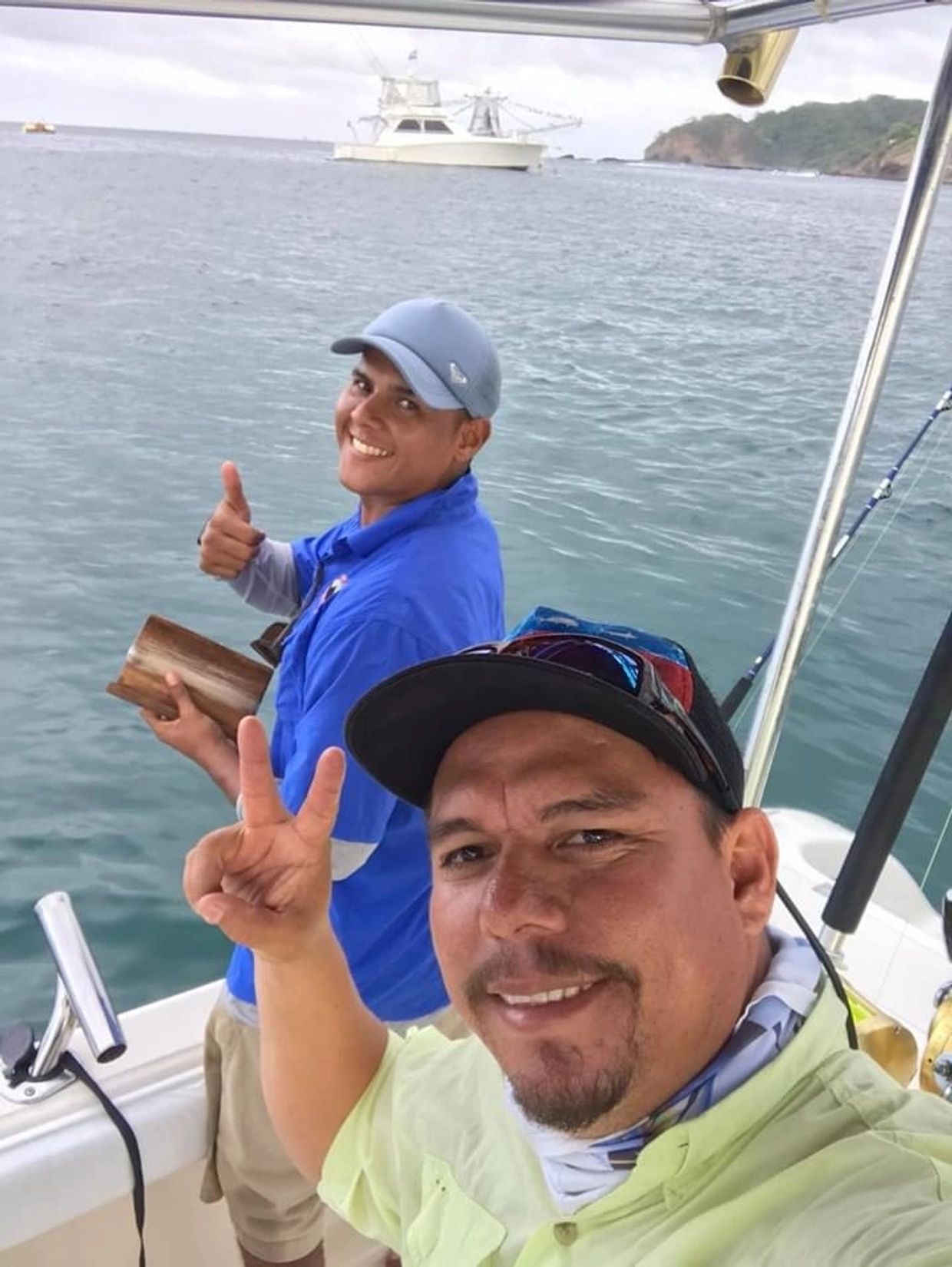 Two men smiling and posing on a boat with water and another boat in the background.