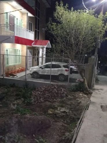 A white car parked in a fenced driveway next to a house at night.