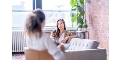 One woman in a chair facing the other woman on the couch having a counseling session.