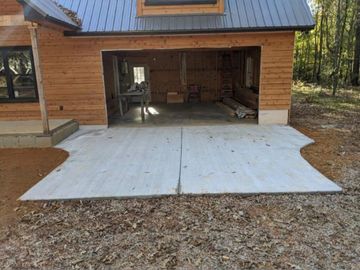 Newly poured concrete driveway dried and cured outside a wooden garage.