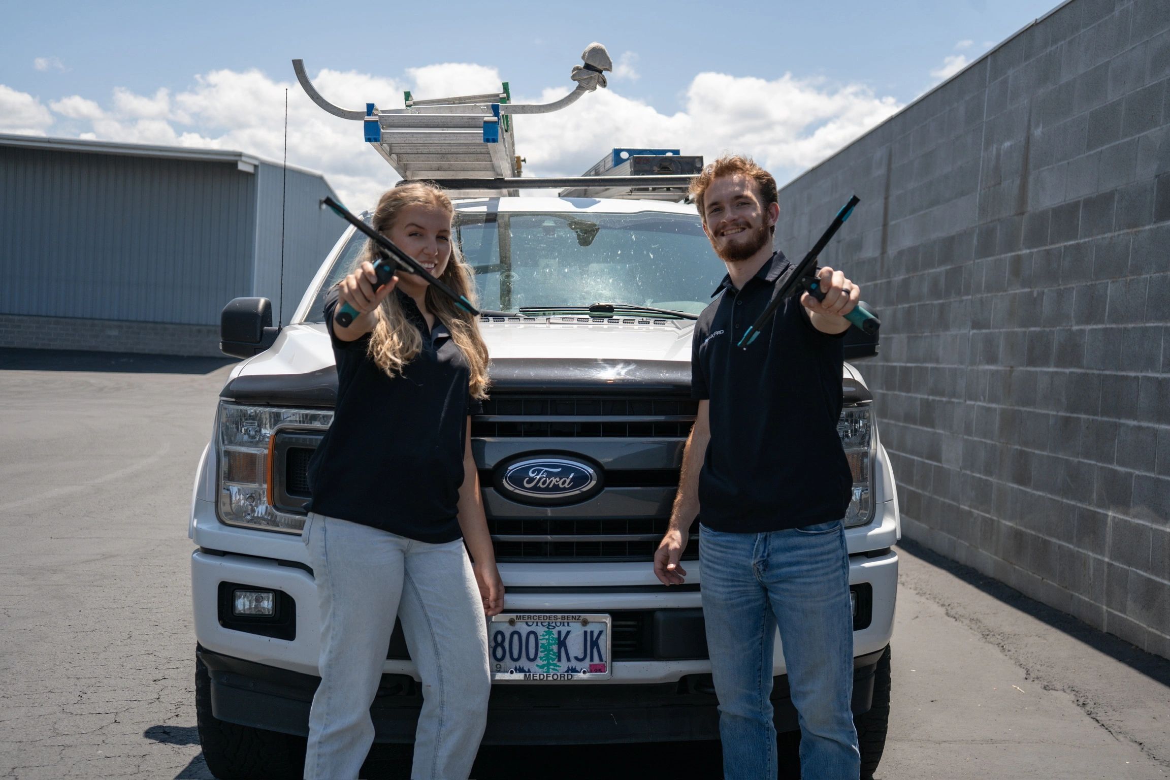 Two people holding window squeegees in front of a white Ford truck.