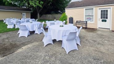 Outdoor wedding party setup with white-covered tables and chairs.
