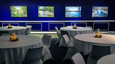 Elegant event space with round tables, white chairs, and nature-themed paintings on deep blue walls.
