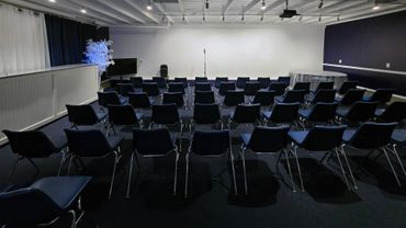 Empty conference room with chairs facing a microphone on stage.