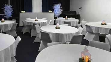 Elegant event room with white-covered tables and chairs, decorated with lantern centerpieces and illuminated plants.