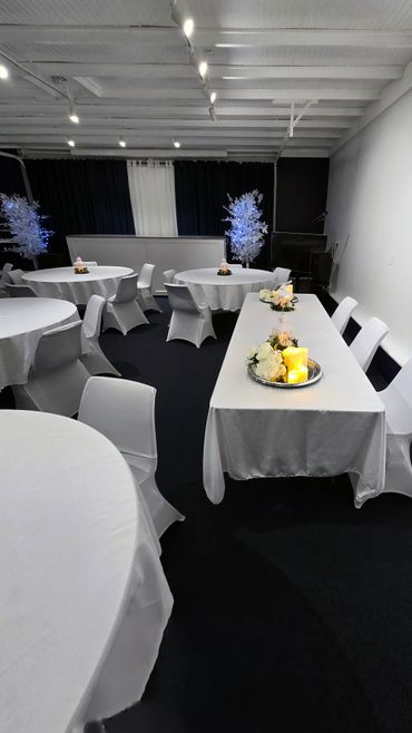 Elegant event room with white tablecloths, chairs, and candle centerpieces.