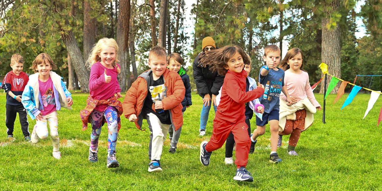 Children joyfully running in a grassy park during a sunny day.