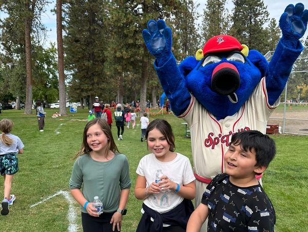 Kids smiling with a blue mascot at a park event.