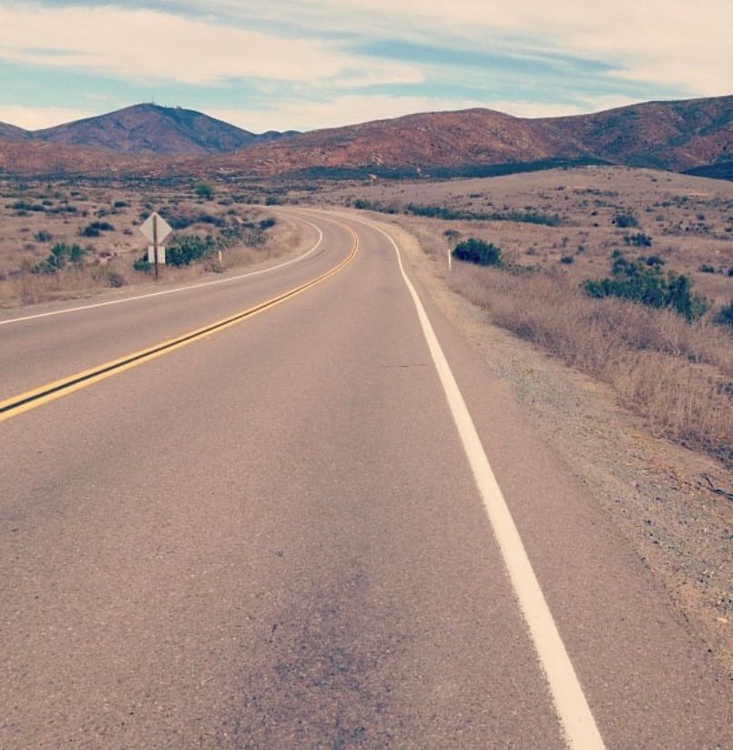 Empty winding road in a dry, mountainous landscape.