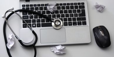 Laptop with crumbled pieces of paper and a stethoscope.