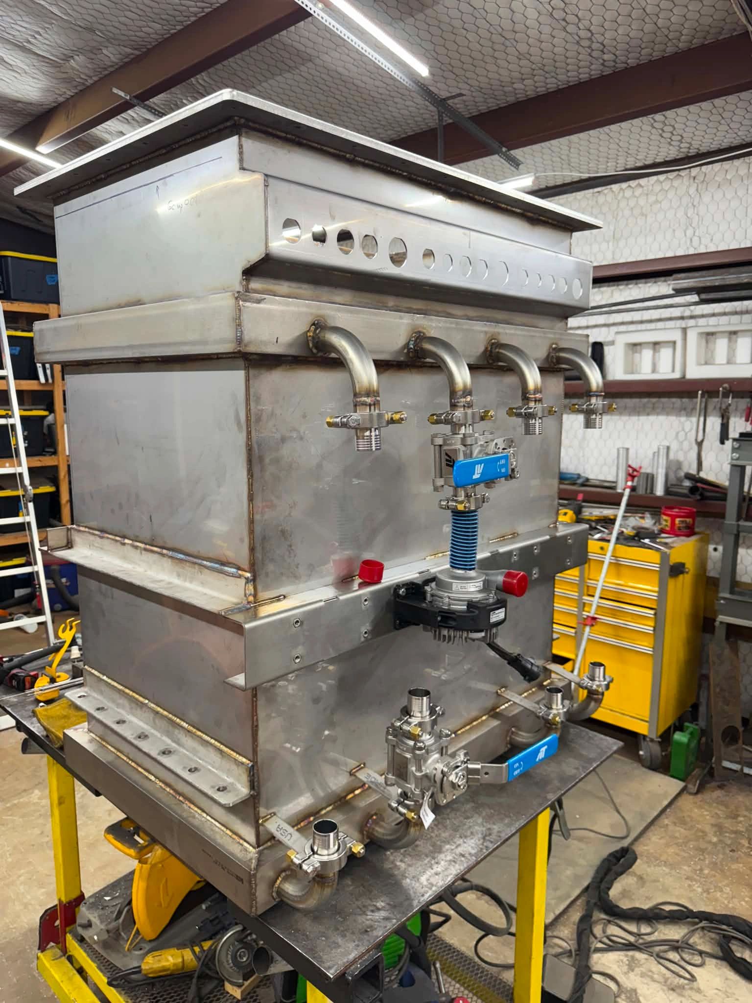 Large industrial metal container with multiple valves and pipes in a workshop.