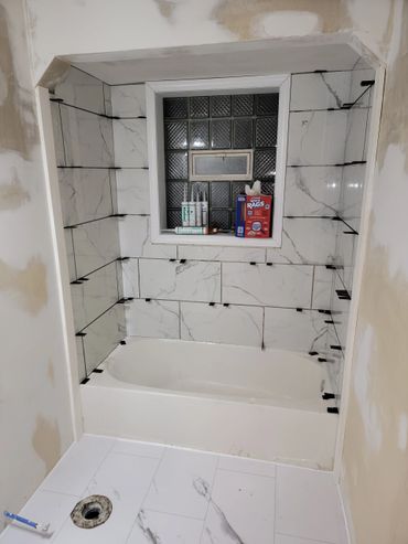 Bathtub area under renovation with marble tiles and window.