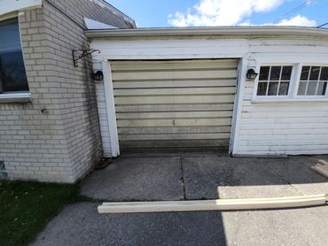 Old garage door with dirty lower panels and wood planks on driveway.